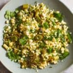 Fresh corn salad with shishito pepers topped with cilantro on a gray plate.