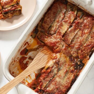 A pan of zucchini parmesan with a wooden spatula in it.