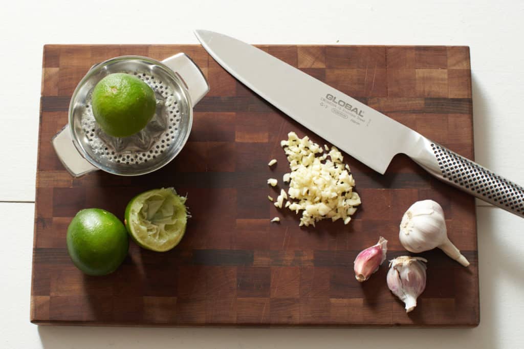 A juicer with a lime, a knife, and garlic on a cutting board.