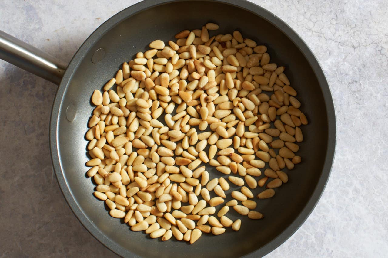 A small skillet with toasted pine nuts.