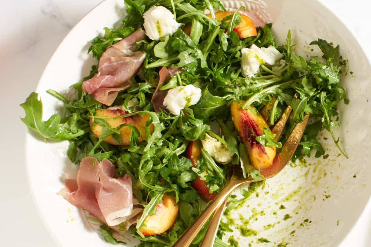 Peach salad in a white bowl with gold serving utensils in it.