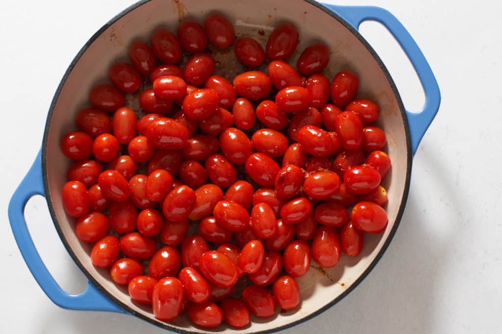 Grape tomatoes and other ingredients in a blue casserole pan.