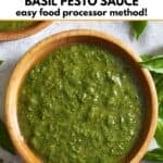 A wooden bowl full of pesto surrounded by fresh basil and garlic cloves.