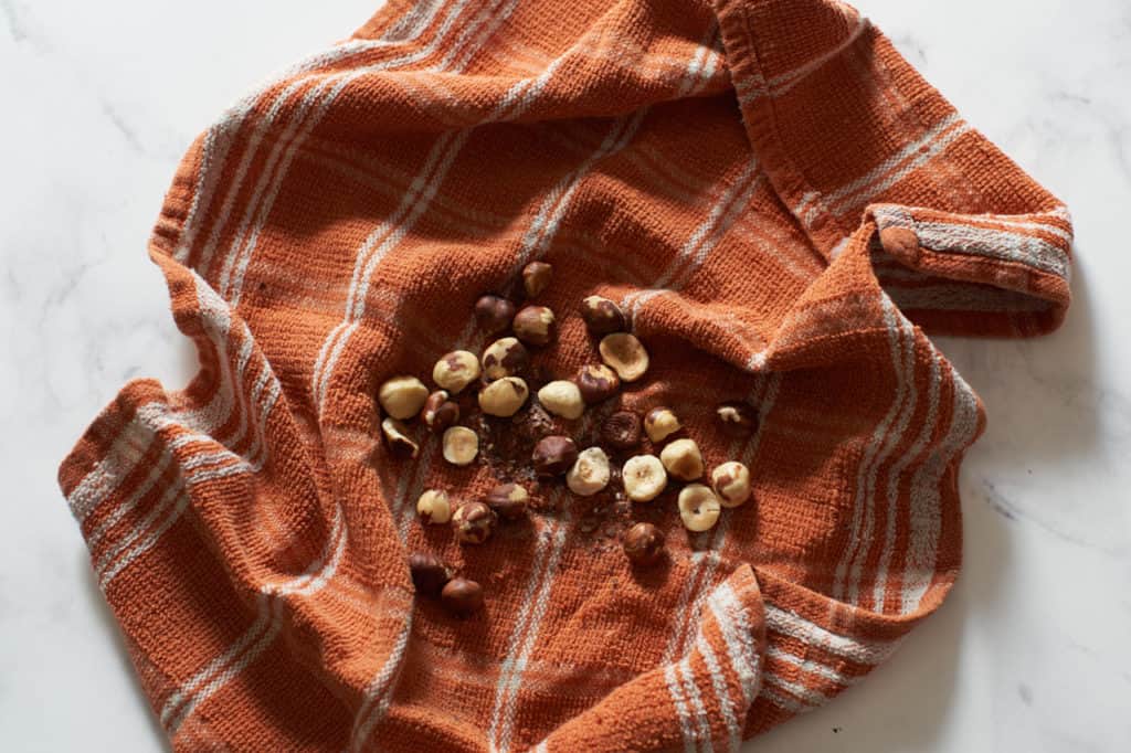 An orange kitchen towel with hazelnuts and their skins.
