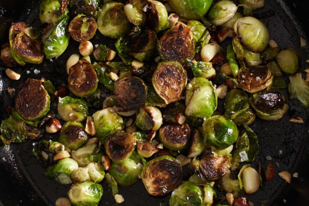 Crispy brussels sprouts in a cast iron pan with hazelnuts and garlic.