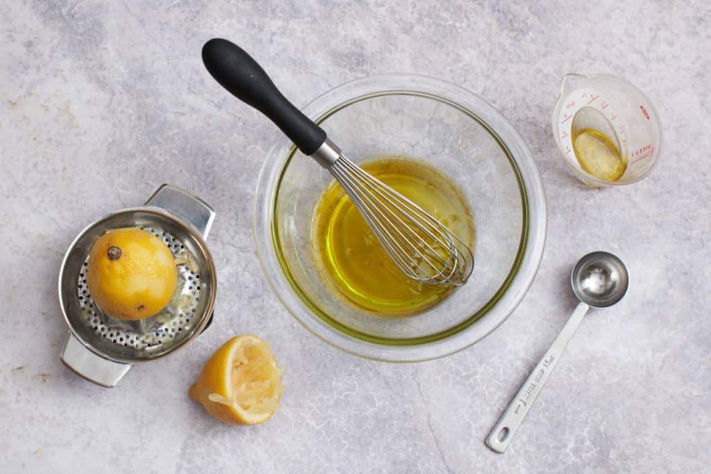 A bowl of lemon vinaigrette surrounded by a juicer, a measuring cup and a measuring spoon.