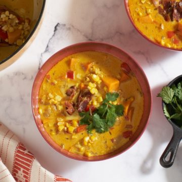 Corn chowder with bacon and sweet potatoes in a red bowl.