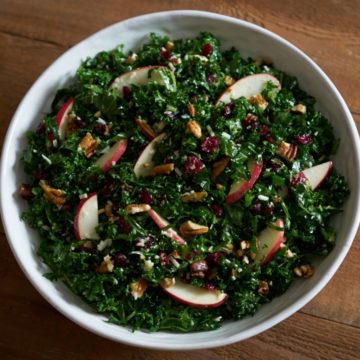 Kale salad with apples, pecans, and cranberries in a white bowl.