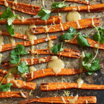 Roasted carrots with tahini sauce and cilantro on a sheet pan.