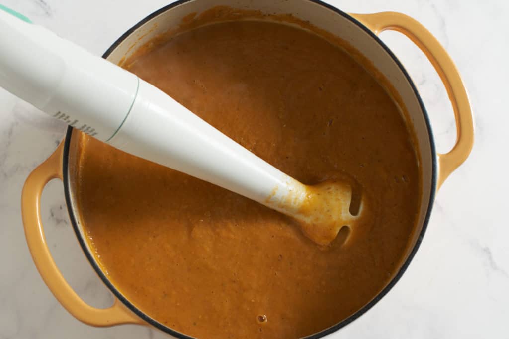 An immersion blender in a dutch oven with sweet potato soup.
