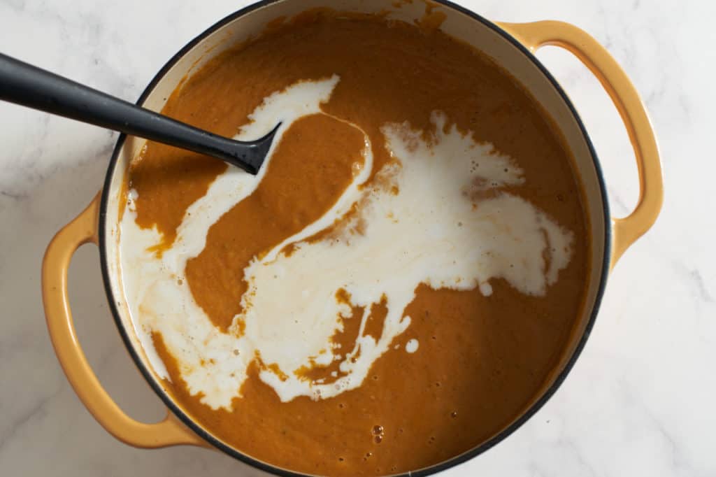 A pot of sweet potato soup with coconut milk drizzled into it.