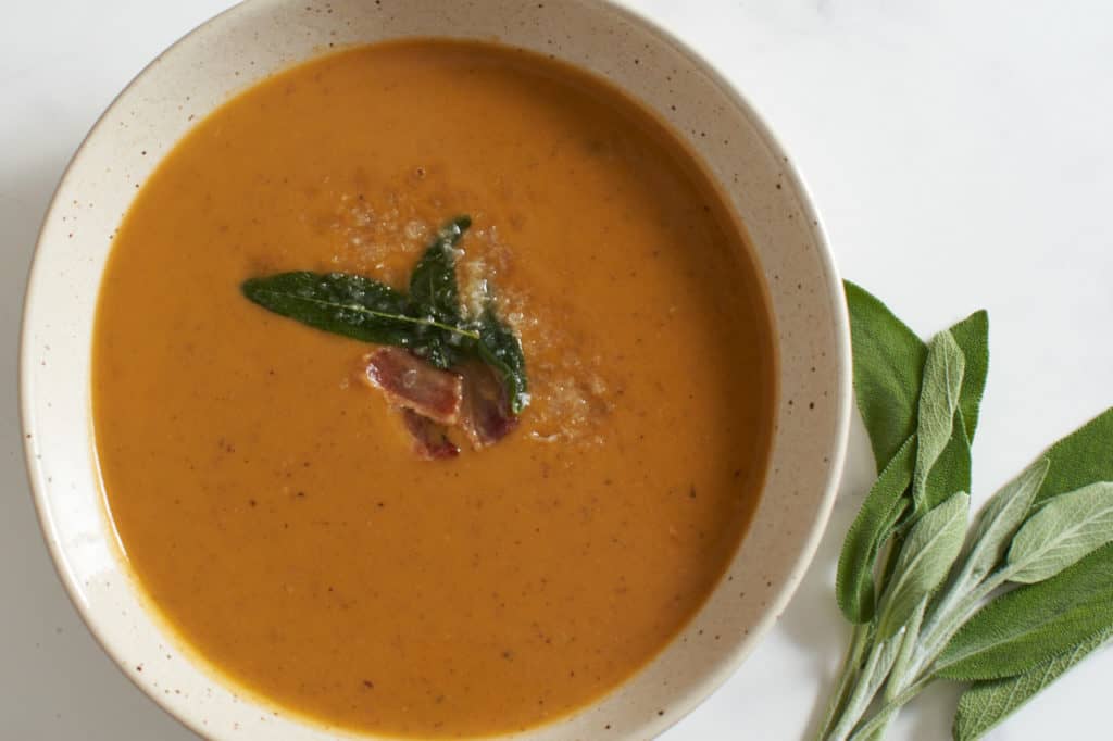 A bowl of sweet potato soup topped with bacon and fried sage leaves.
