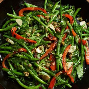 Fresh green bean salad with red peppers, capers and herbs in a skillet.