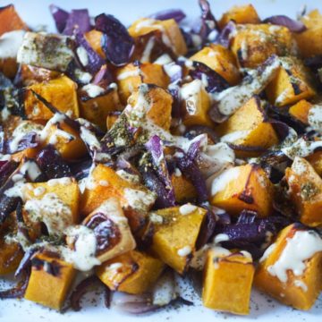 Roasted butternut squash and red onions topped with tahini and za'atar on a white plate.
