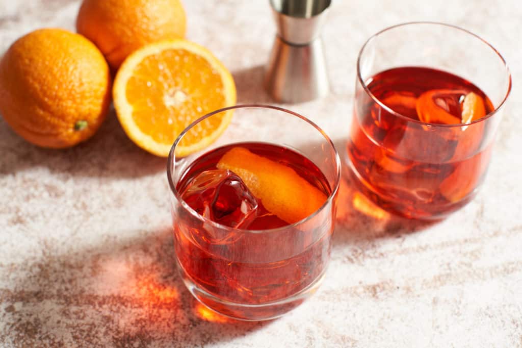 Two Negroni cocktails with oranges and a cocktail jigger.