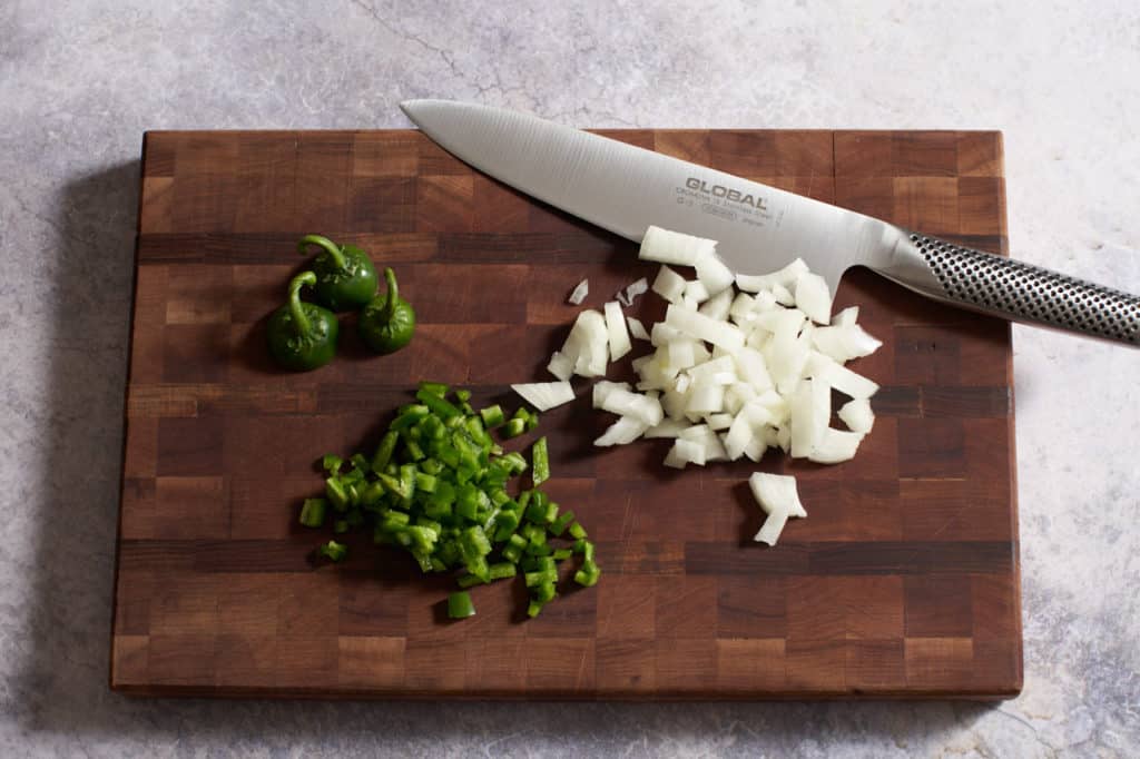 A knife on a cutting board with chopped onions and jalapeños.