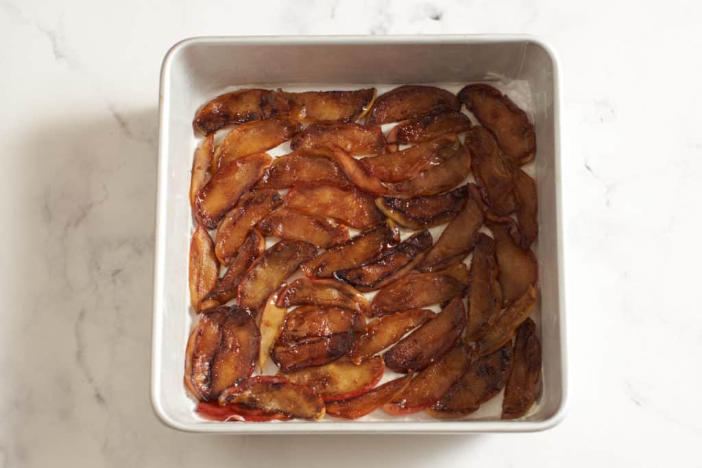 A square cake pan with caramelized sliced apples in the bottom.