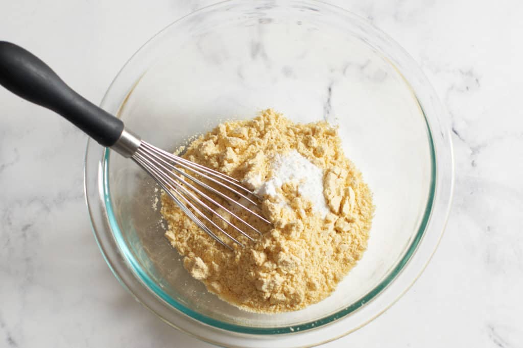A bowl with cornmeal, baking powder and a whisk.
