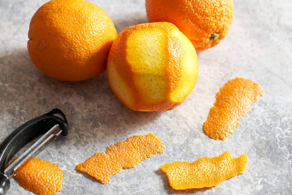 Oranges, strips of orange zest, and a vegetable peeler.