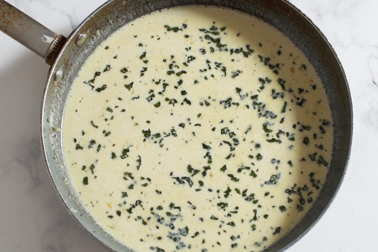 Sage and parmesan cream sauce in a skillet.