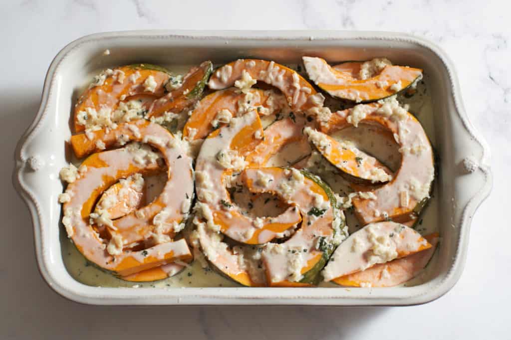 Kabocha squash in a baking dish with sage cream sauce poured over it.
