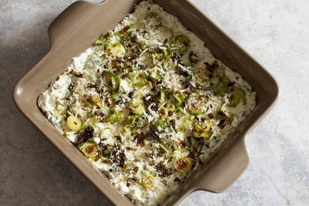 Roasted brussels sprouts dip in a brown square pan ready to be baked.