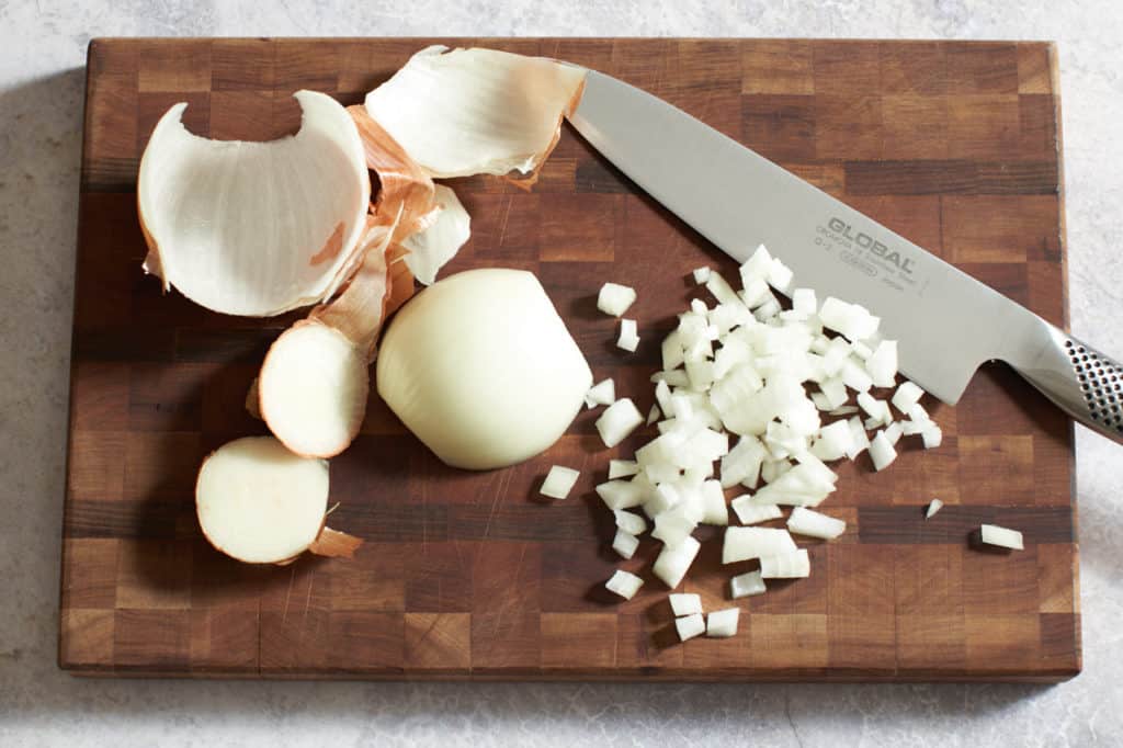 A knife on a wooden cutting board with chopped onion.