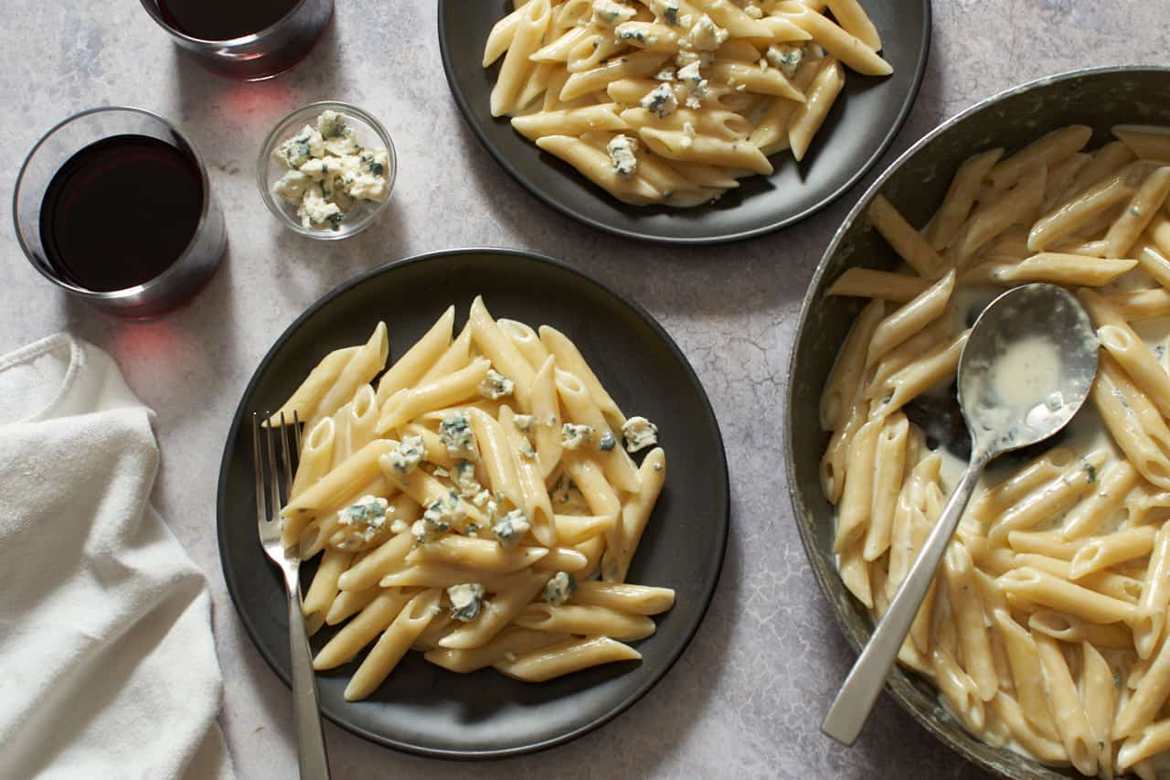 Gorgonzola pasta on two black plates and in a skillet, two glasses of wine and a napkin are to the left.