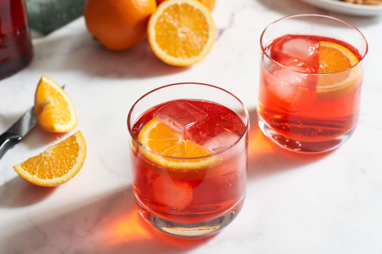 Two campari and soda cocktails garnished with orange wedges.