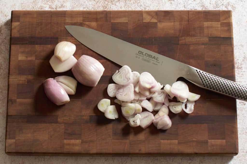 Sliced shallots on a cutting board with a knife.