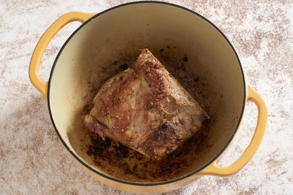 A yellow Dutch oven containing seared pork shoulder.