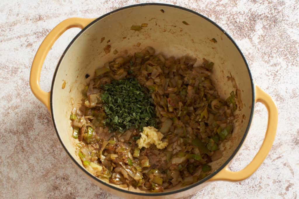 A yellow Dutch oven with cooked leeks and shallots topped with chopped sage and garlic.