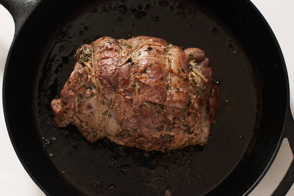 A seared leg of lamb in a cast iron skillet.