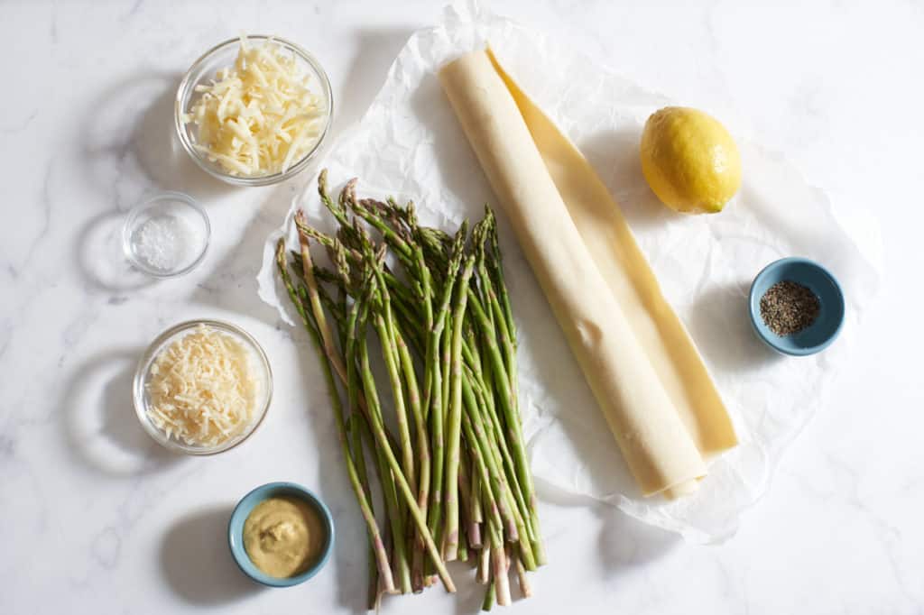 Fresh asparagus, puff pastry, a lemon, and small bowls of grated cheeses, salt, pepper and Dijon mustard.
