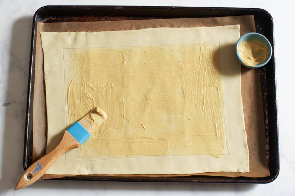A sheet of puff pastry that has been brushed with Dijon mustard.