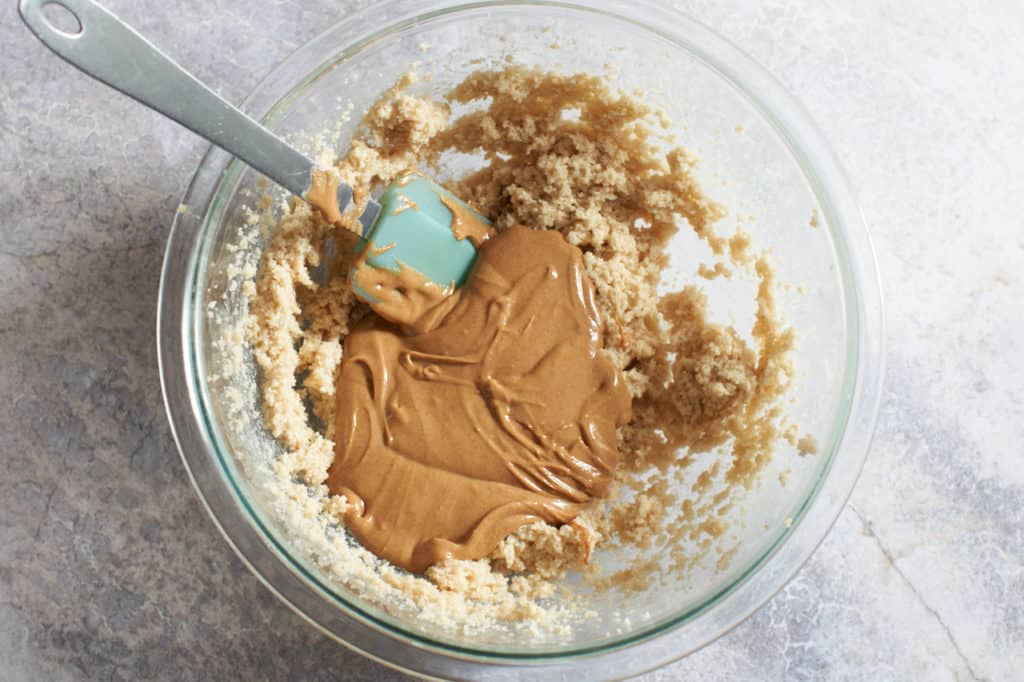 A spatula in a bowl filled with creamed butter and sugar, and natural peanut butter.