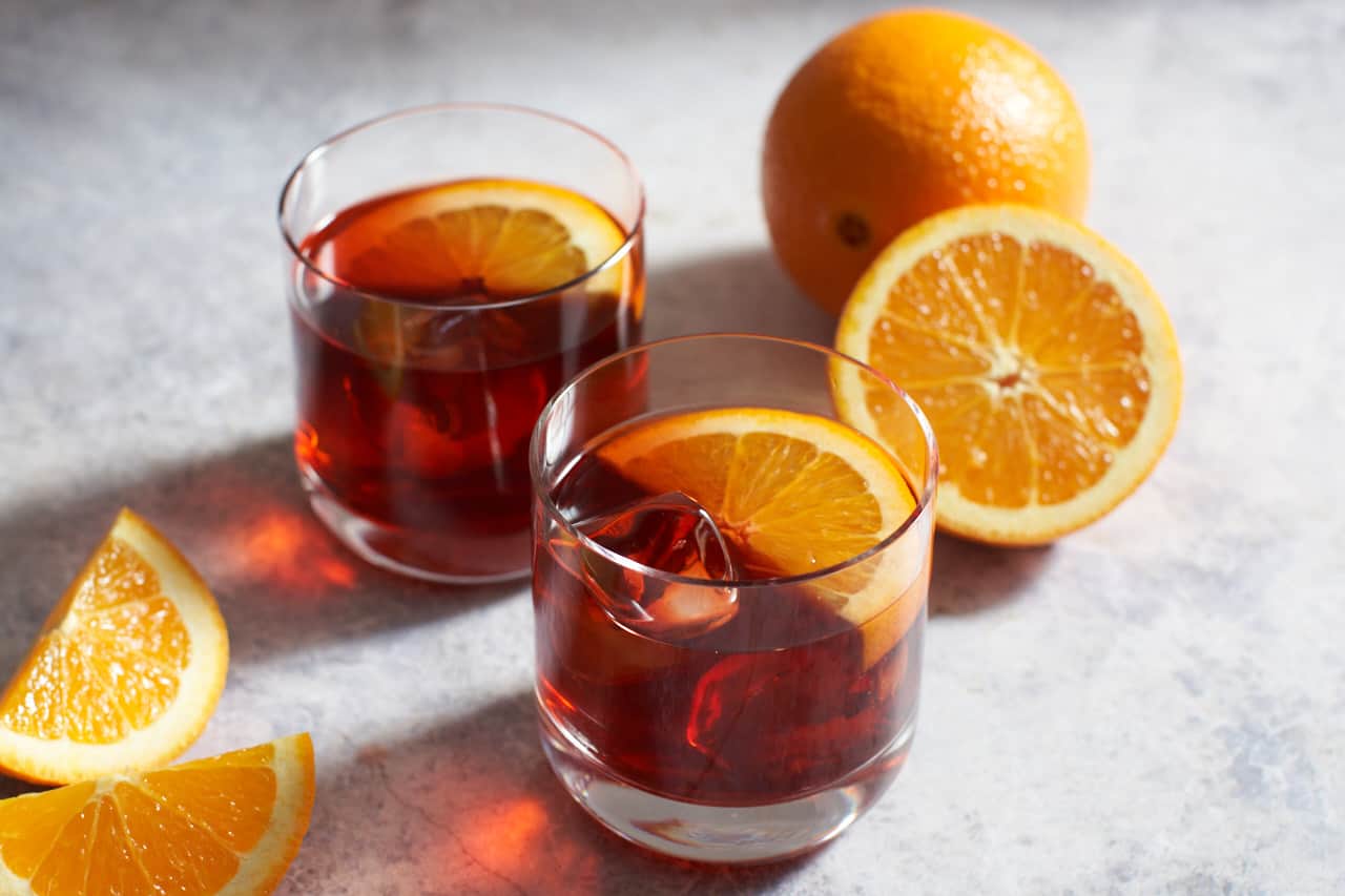 Two mezcal negronis next to sliced oranges.