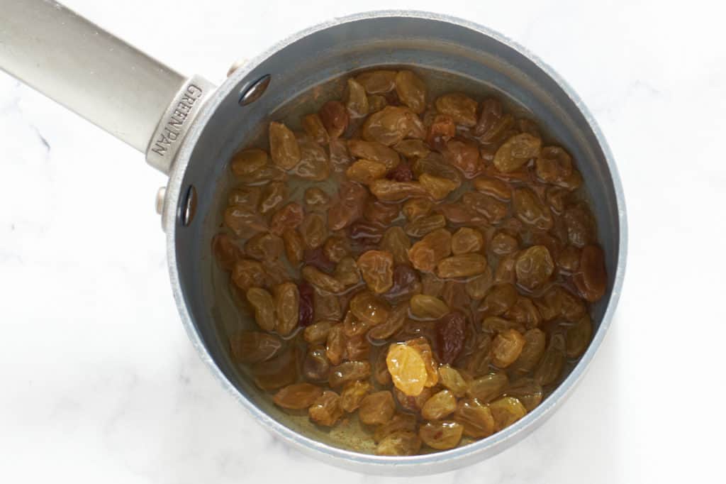 A small sauce pan with golden raisins and rum.
