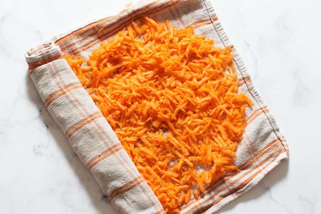 A kitchen towel full of shredded carrots partially rolled up.