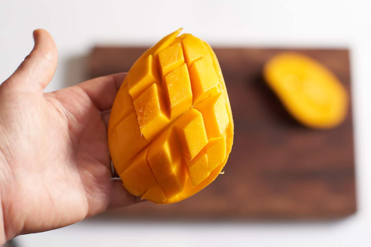 A woman's hand holding half a mango that has been scored and bent backwards so the slices can be easily removed.