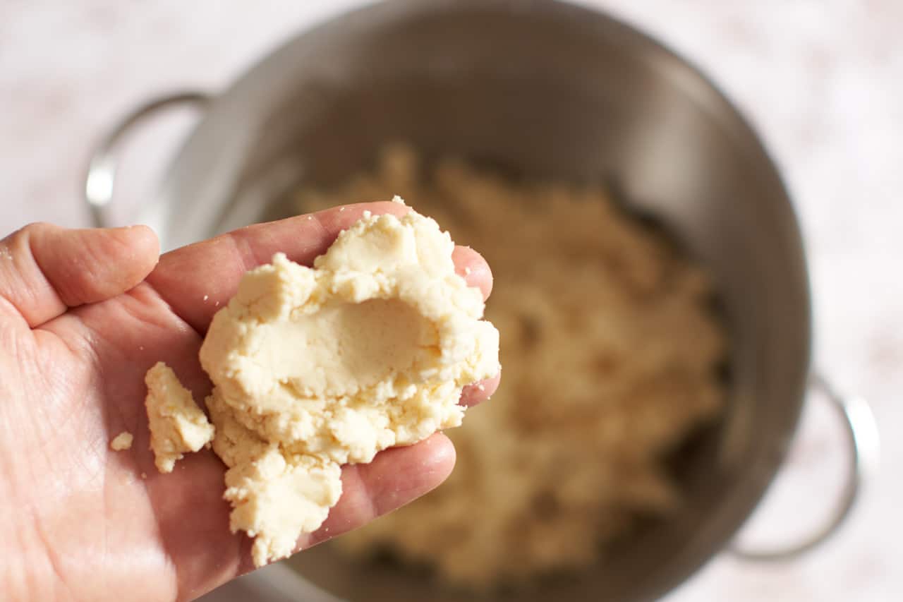 A woman's hand holding some cookie batter with an indent in it made by her thumb.