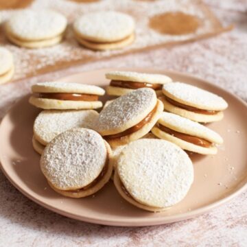 Alfajores cookies dusted with powdered sugar on a pink plate.