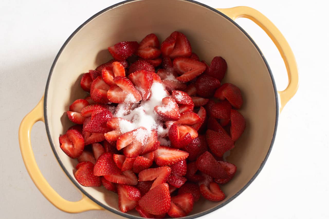 A yellow Dutch oven holds sliced strawberries topped with sugar.