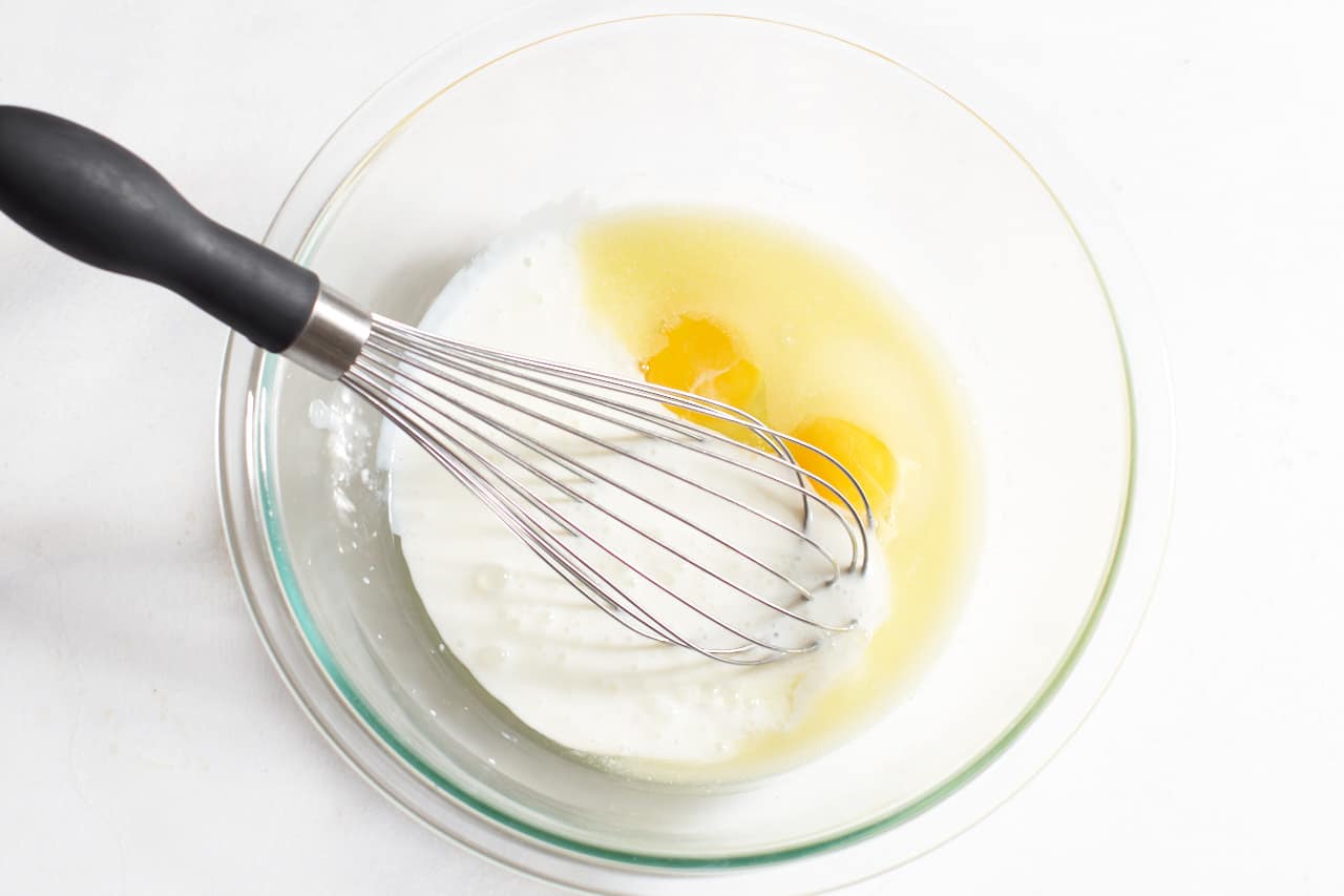 A whisk in a glass bowl containing buttermilk, melted butter and eggs.