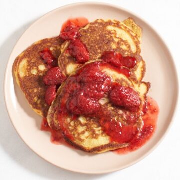 Three cornmeal pancakes on a pink plate topped with strawberry compote.