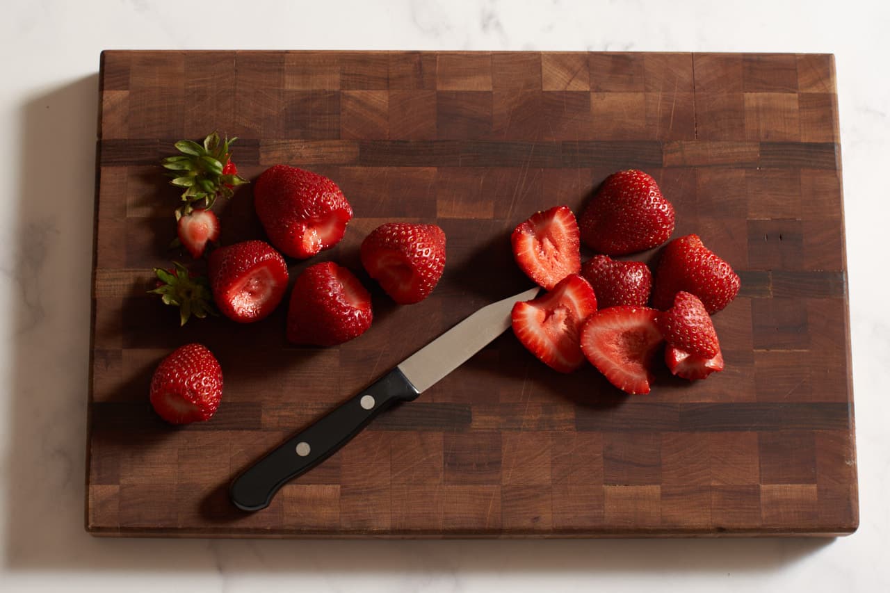 Sliced strawberries and a paring knife on a wooden cutting board.