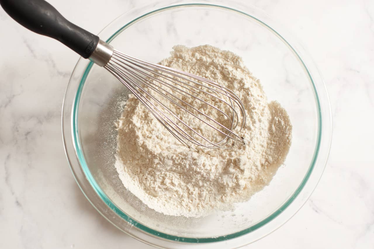A whisk in a glass bowl of flour.