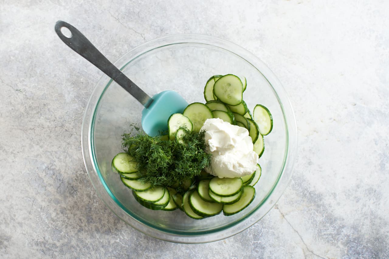 Lightly pickled cucumber slices in a glass bowl with sour cream and chopped dill.