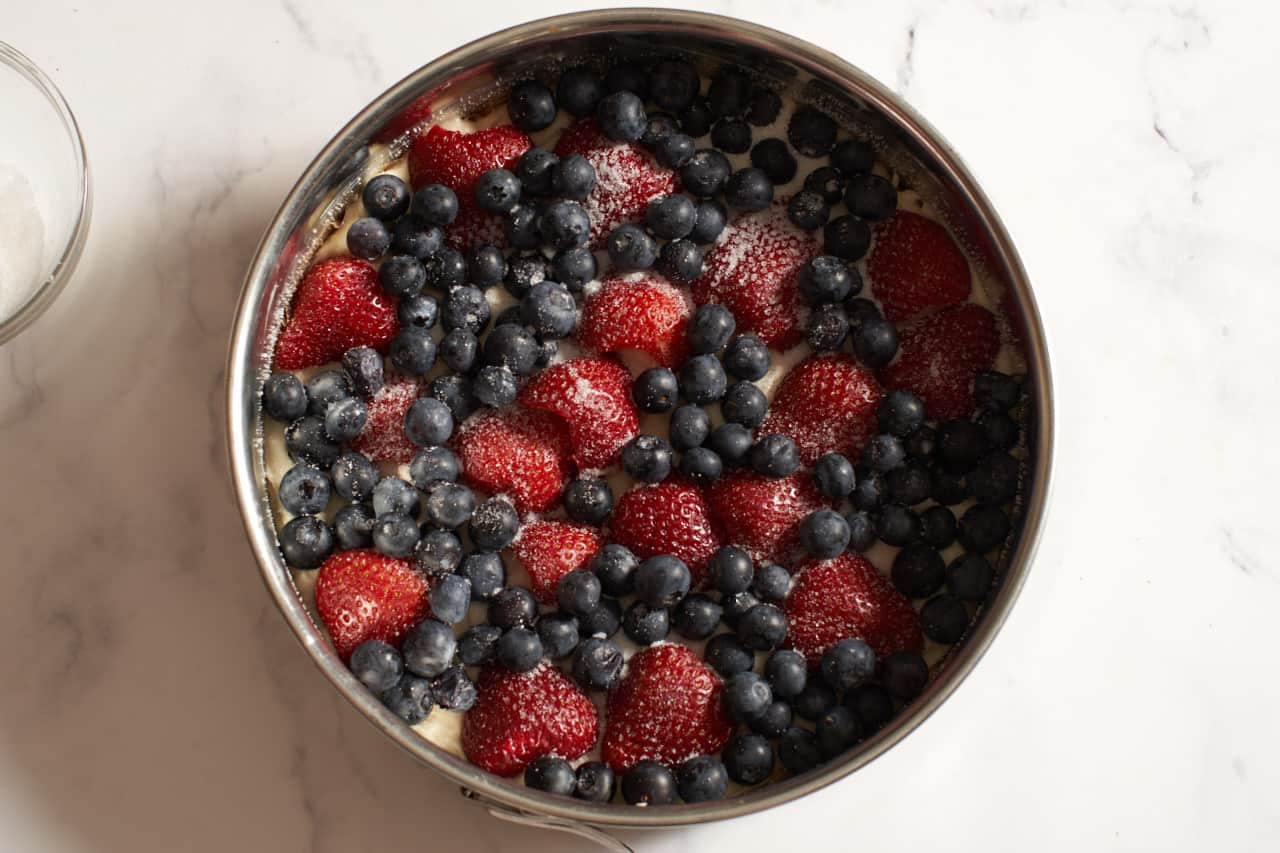 Mixed berry cake batter topped with berries and sugar in a springform pan.