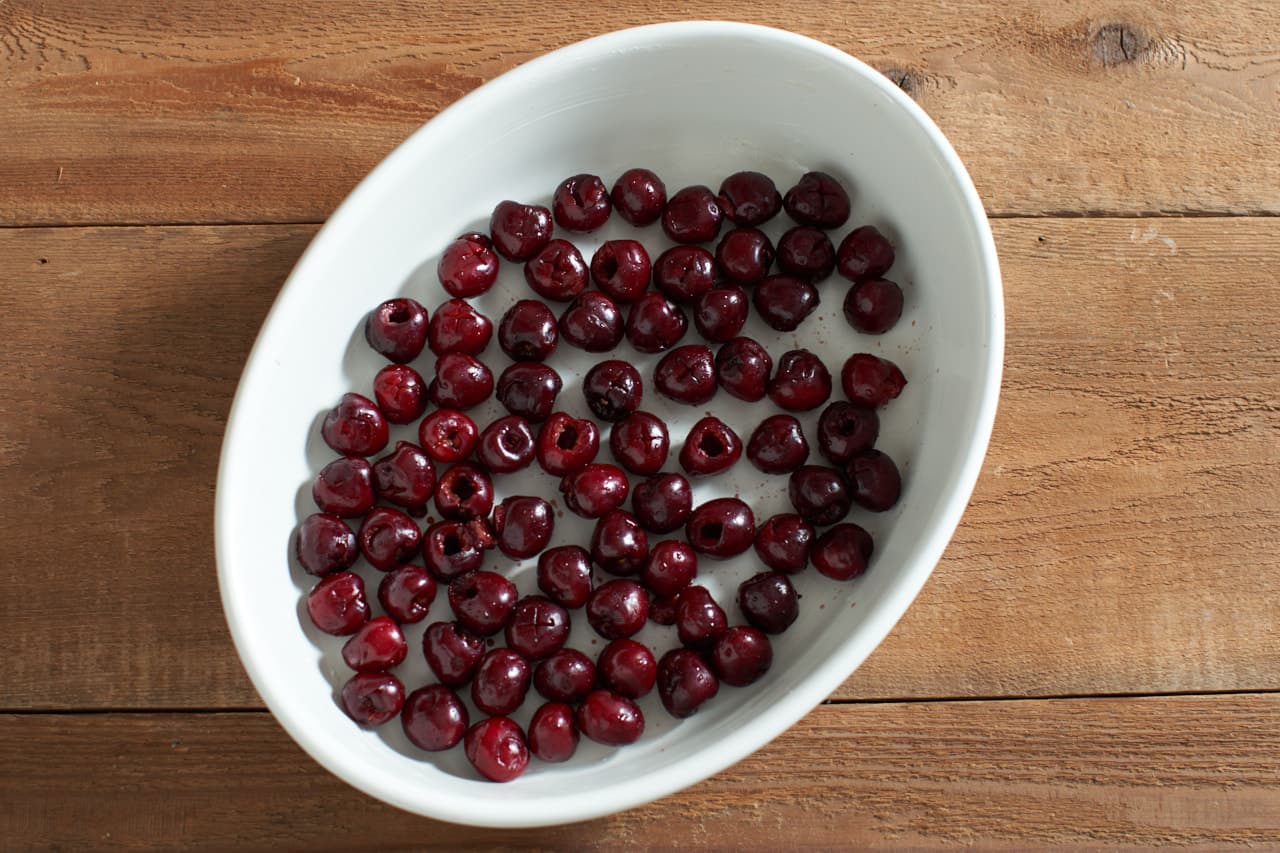 A white oval dish that has been buttered with fresh cherries lining the bottom.